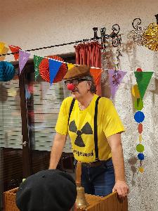 Ein großer Mann mit gelben T-Shirt, Hosenträgern, einer grossen Brille, roter Clownsnase und braunem Barrett am Rednerpult