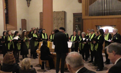 Der Frauenchor des MGV singt in der evangelischen Kirche in Schönau, begleitet von einer Frau am Klavier um das sich der Chor postiert hat. Der Dirigent steht neben dem Klavier.