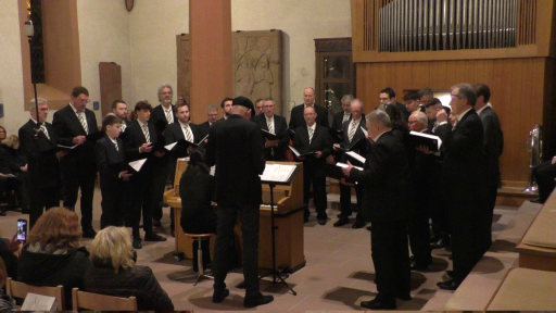 Ein Männerchor singt in der evangelischen Kirche in Schönau. Der Dirigent steht dabei neben einem Klavier, die Pianistin begleitet den Chor.