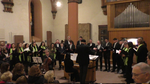 Ein gemischter Chor singt in der evangelischen Kirche in Schönau. Der Dirigent steht dabei neben einem Klavier, die Pianistin begleitet den Chor. 