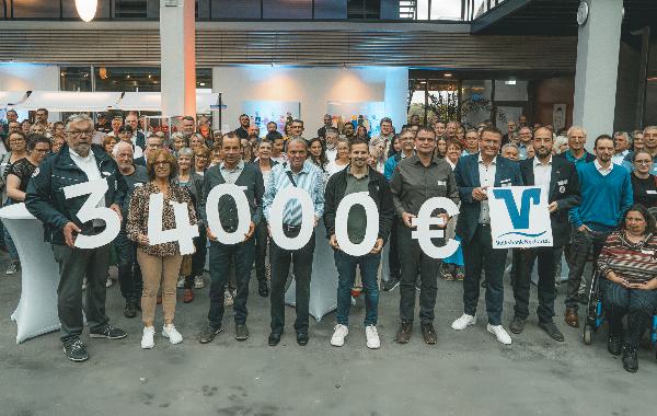 Ein Gruppenbild vor einem Gebäude. Im Vordergrund halten mehrere Personen Zahlen in den Händen, die zusammen 34000€ ergeben.